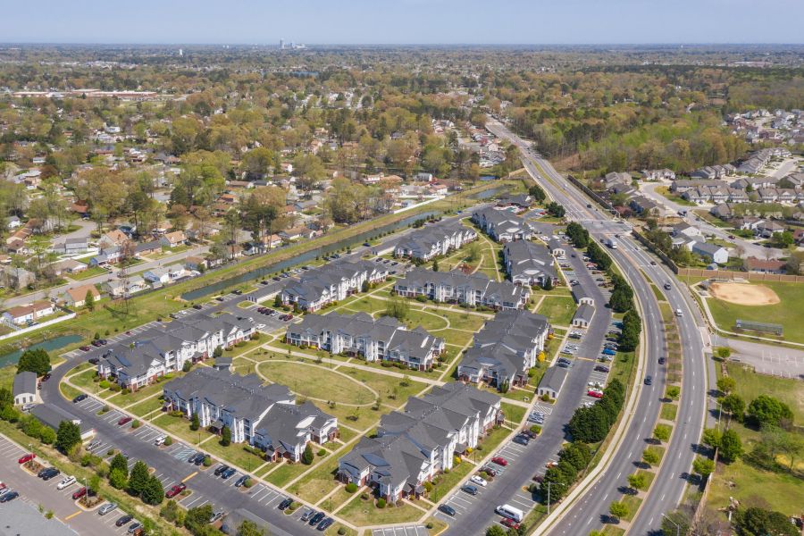 Aerial view of a suburban apartment complex surrounded by roads, trees, and nearby residential areas.