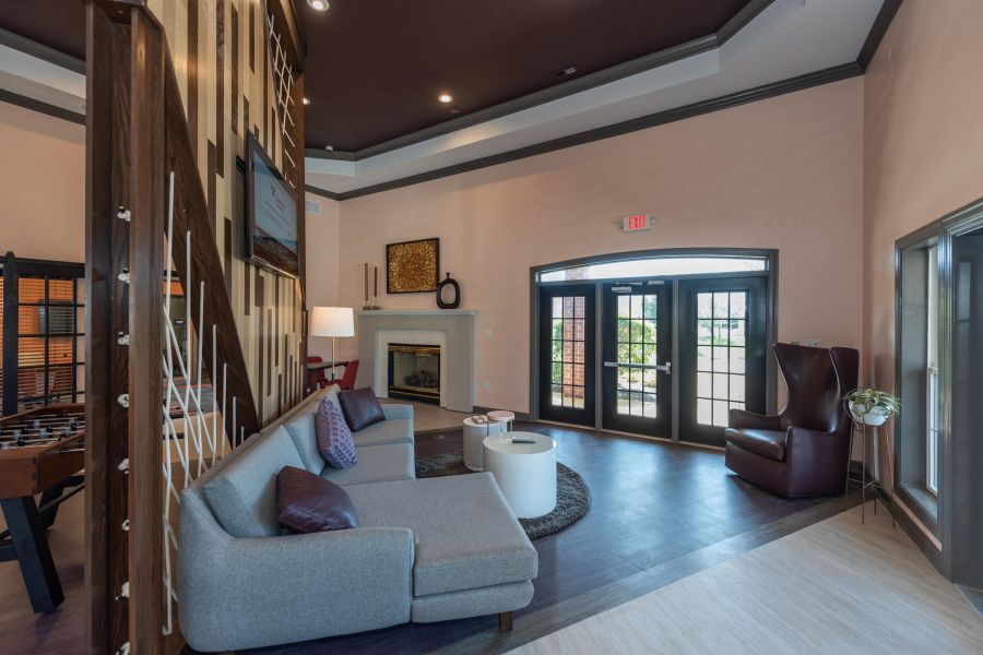 Attain on 5th apartment homes with Modern lounge with gray sectional sofa, armchair, game table, fireplace, and double glass doors.