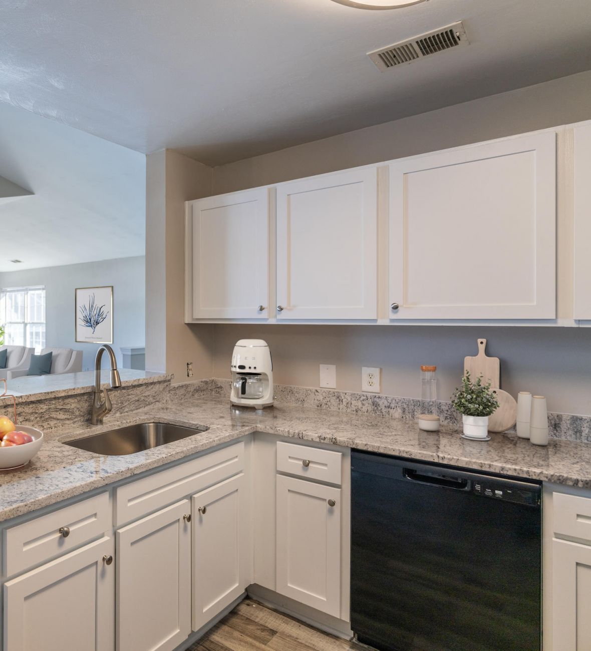 Attain on 5th apartment homes with Modern kitchen with white cabinets, granite countertops, and a view into a bright living room with a balcony.