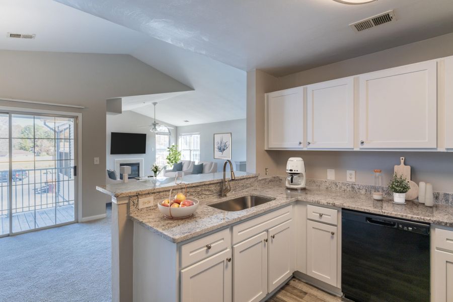 Attain on 5th apartment homes with Modern kitchen with white cabinets, granite countertops, and a view into a bright living room with a balcony.