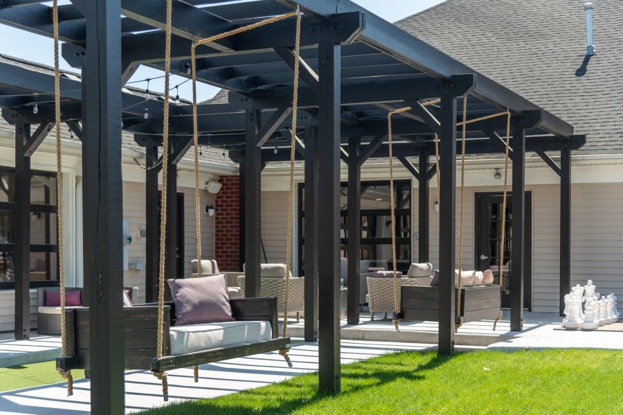 Attain on 5th apartment homes with Outdoor patio with black pergola, wooden swings, cushioned chairs, and large chess pieces on the lawn.