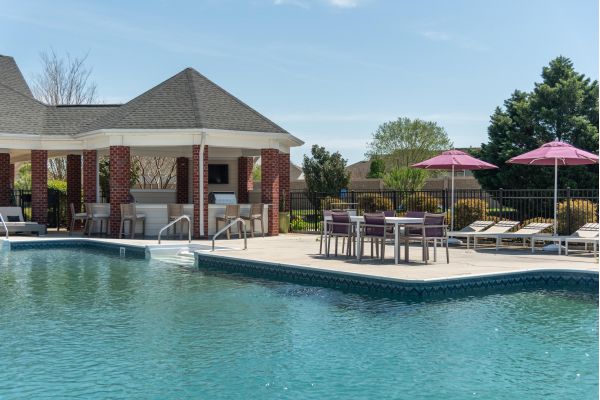 Attain on 5th apartment homes with Outdoor pool area with lounge chairs, umbrellas, dining tables, and a covered pavilion on a sunny day.