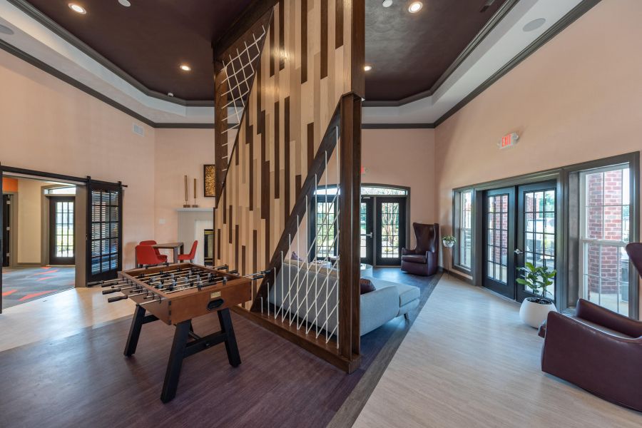 Attain on 5th apartment homes with Spacious lounge area with a foosball table, modern seating, large windows, and decorative wooden divider.