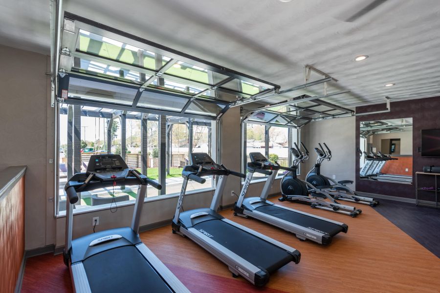 Attain on 5th apartment homes with Modern gym with treadmills and ellipticals near large windows and an open garage-style door.