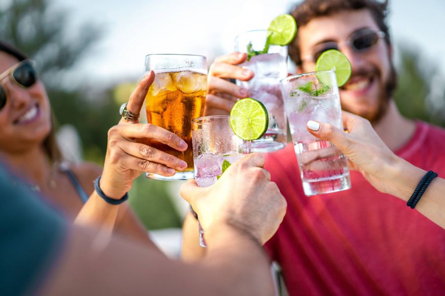 Attain on 5th apartment homes with Friends clinking glasses with drinks and lime slices outdoors, smiling and enjoying a sunny day.