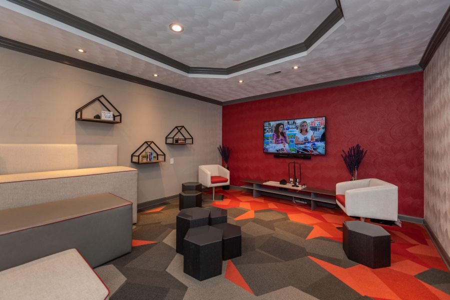 Attain on 5th apartment homes with Modern lounge with geometric carpet, wall-mounted TV, shelves, beige seating, and two white chairs.
