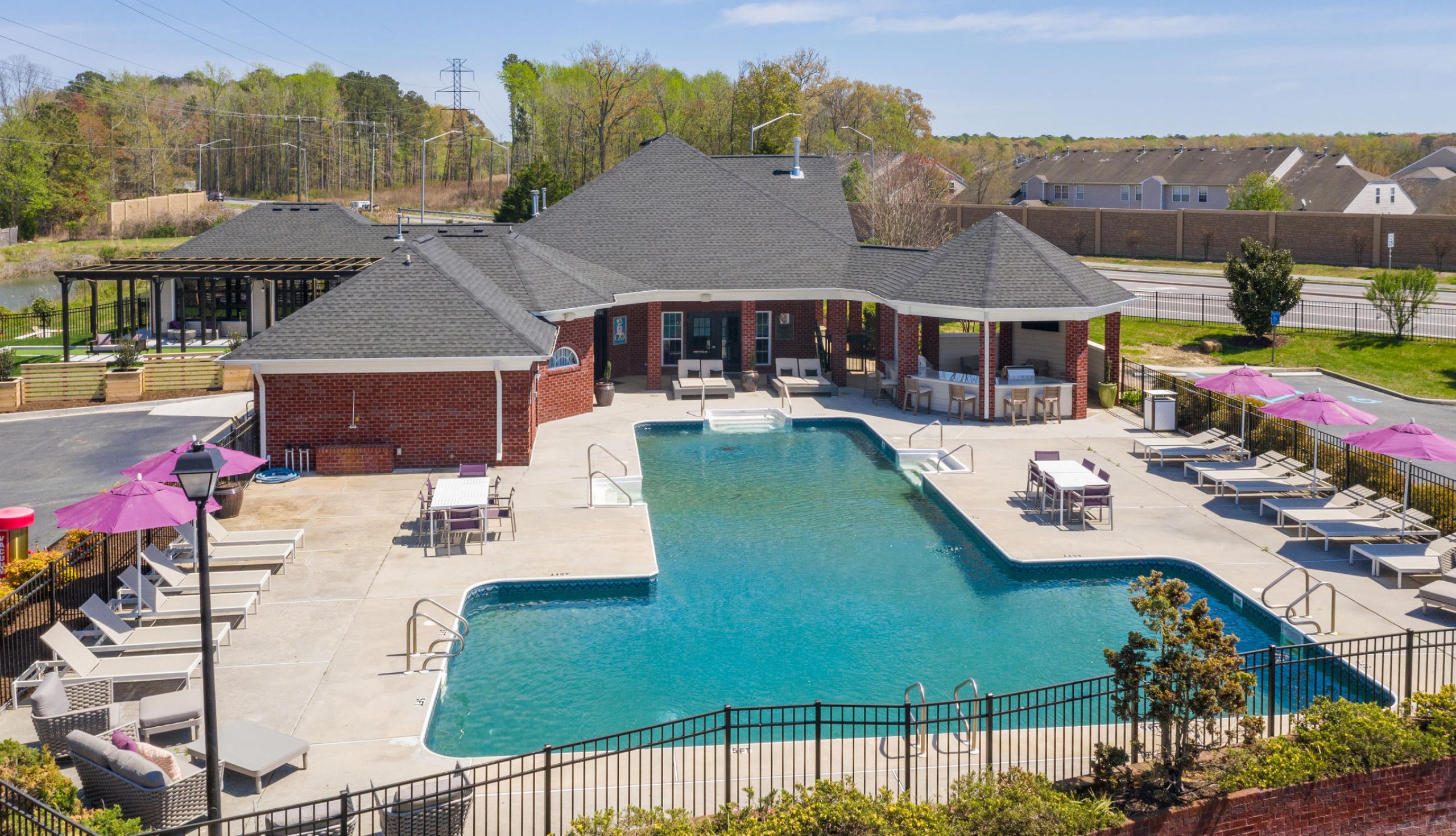 Rectangular outdoor pool with lounge chairs, umbrellas, and a brick clubhouse on a sunny day.