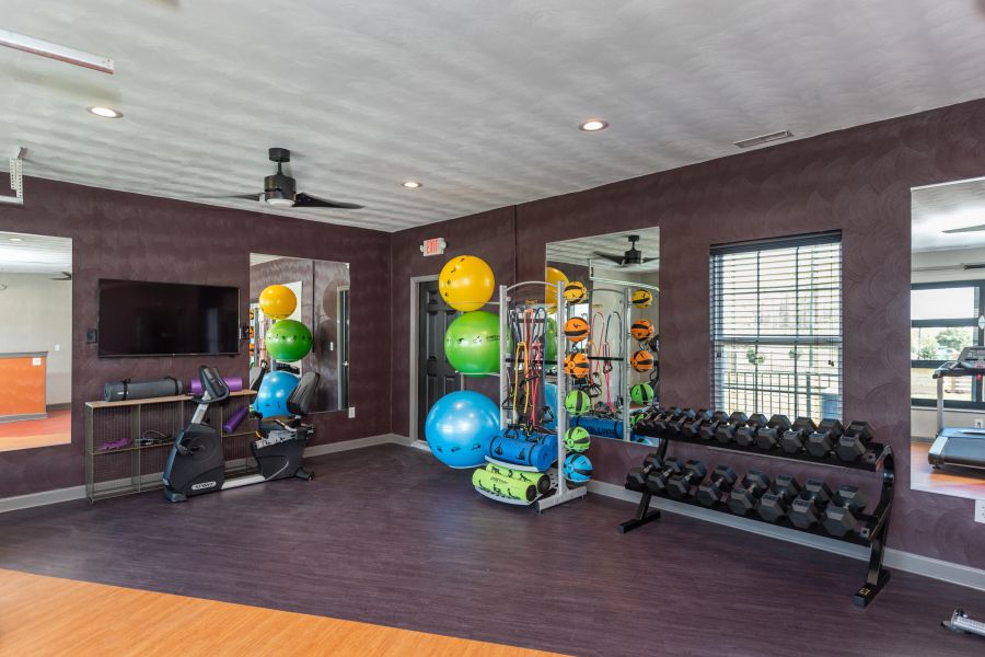 Attain on 5th apartment homes with Modern gym room with exercise balls, dumbbells, resistance bands, and a stationary bike near a large mirror.