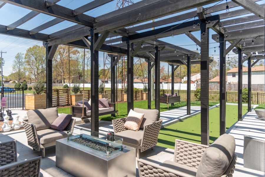 Attain on 5th apartment homes with Outdoor patio with cushioned seating, fire table, and overhead pergola on artificial grass lawn.