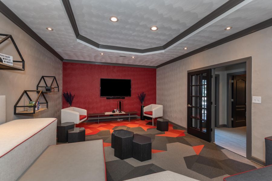 Attain on 5th apartment homes with Modern lounge with red accents, geometric carpet, wall-mounted TV, chairs, and floating shelves.