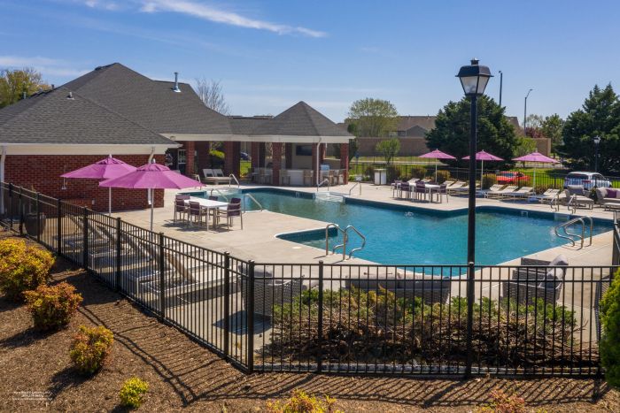Attain on 5th apartment homes with Outdoor swimming pool with lounge chairs, tables and purple umbrellas, surrounded by a black metal fence.