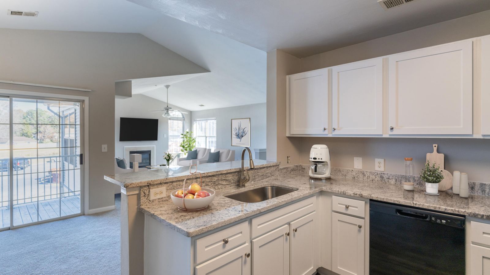 Modern kitchen and living area with white cabinets, stainless steel appliances, and a large island. Cozy seating area with a sofa and rug in the background. Bright and inviting atmosphere.