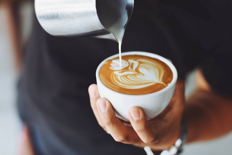 Attain on 5th apartment homes with Hand holding a cup of coffee with latte art as milk is being poured into it.