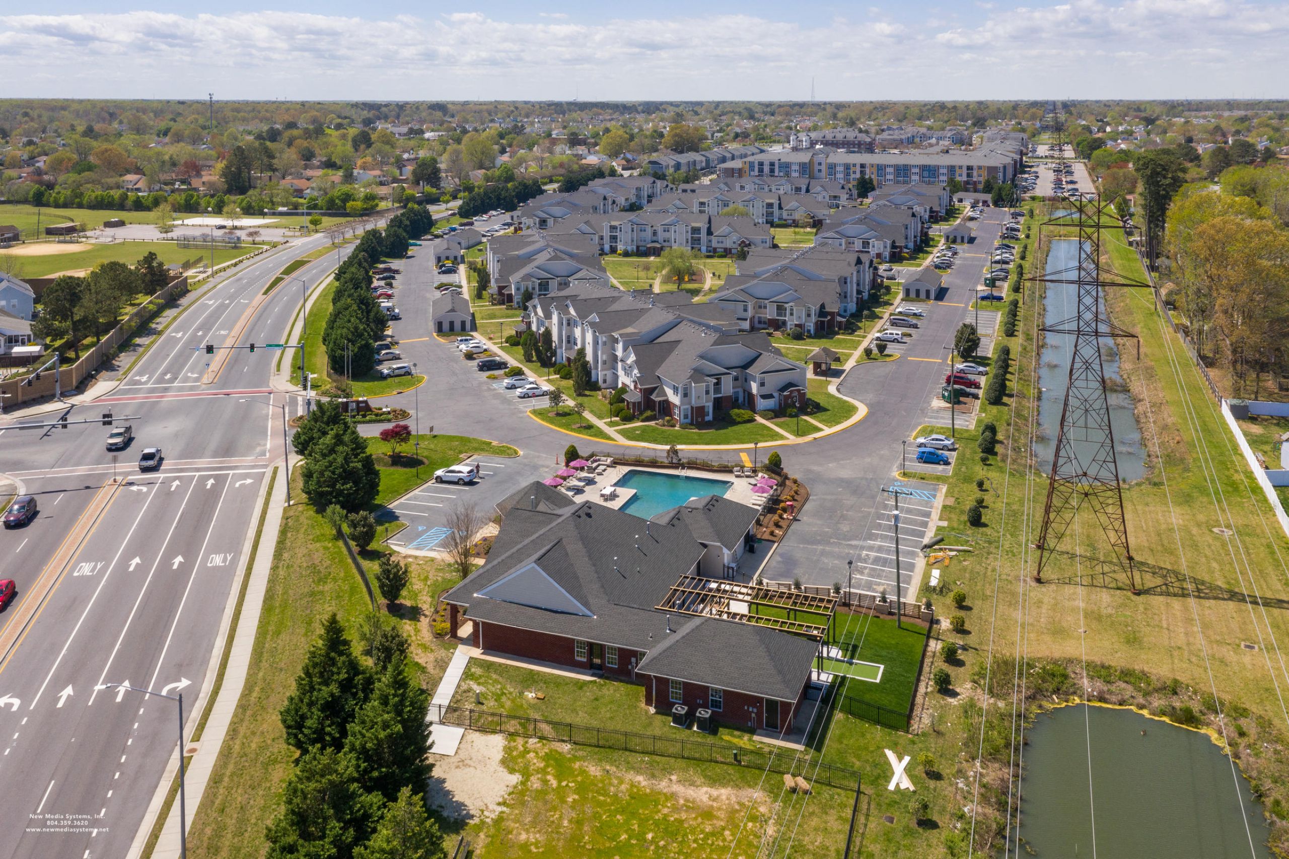 Attain on 5th apartment homes with Aerial view of a suburban apartment complex with parking lots, pool, and nearby roads under a partly cloudy sky.