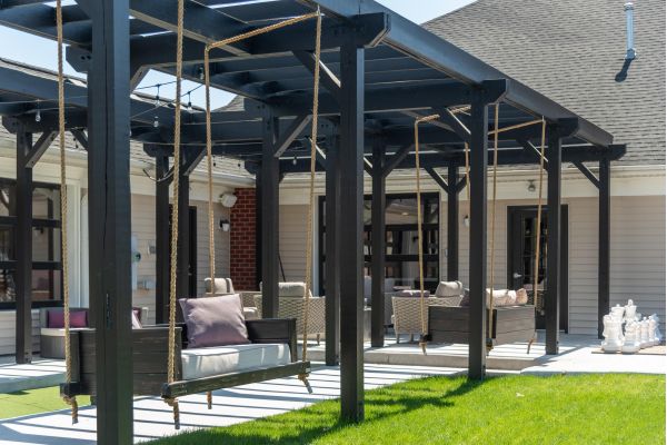 Attain on 5th apartment homes with Outdoor patio with black pergola, wooden swings, cushioned chairs, and large chess pieces on the lawn.