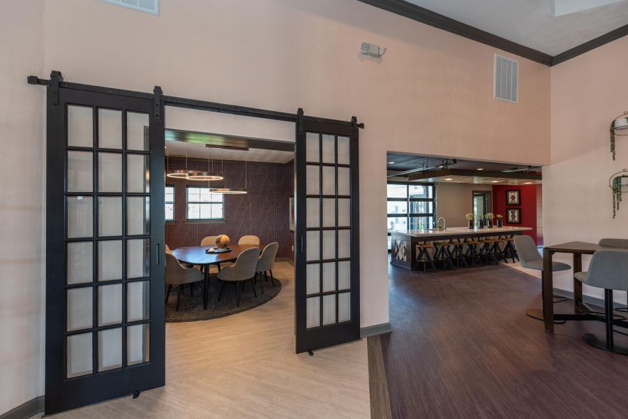 Attain on 5th apartment homes with Sliding glass doors open to a modern meeting room with a round table and chairs, next to a dining area.